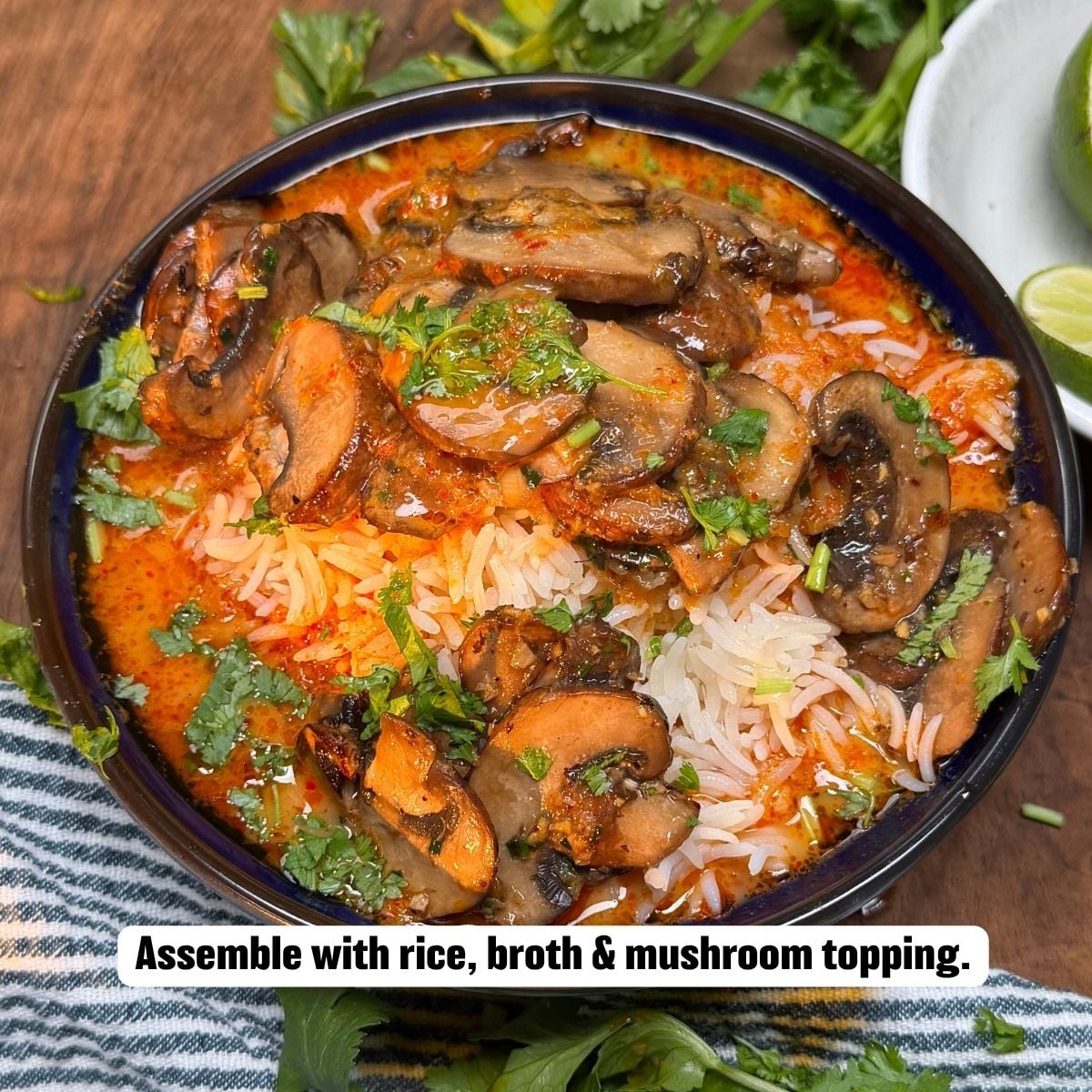 A top-down view of a serving bowl filled with rice, red curry broth, and sautéed mushrooms, garnished with fresh cilantro and served alongside lime wedges.