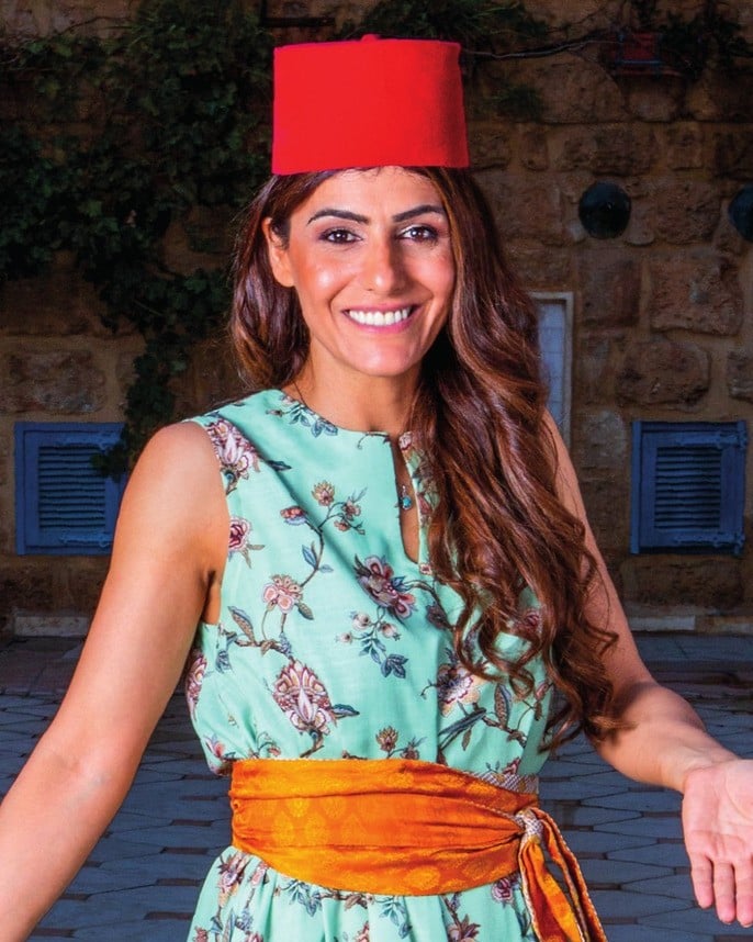 Samira Kazan smiling in a Lebanese courtyard, wearing a red fez